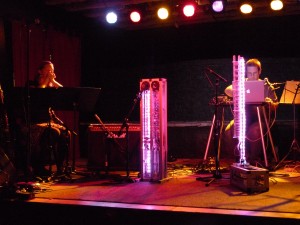 Troy Rogers performs behind the illuminated pink columns of the robotic musical instruments AMI and CARI, which form Expressive Machines Musical Instruments' (EMMI) MARIE, with Dana Jessen of the EAR Duo at the Southern in Charlottesville, VA