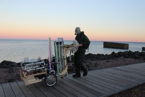 Robot Rickshaw: a cart full of robotic musical instruments piloted by a lunatic in a hazmat suit+teddy bear, being walked along the Lakewalk in Duluth, MN. Photo credit: Melissa Maki