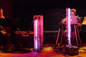 Troy Rogers performs behind the illuminated pink columns of the robotic musical instruments AMI and CARI, which form Expressive Machines Musical Instruments' (EMMI) MARIE, with Dana Jessen of the EAR Duo at the Southern in Charlottesville, VA